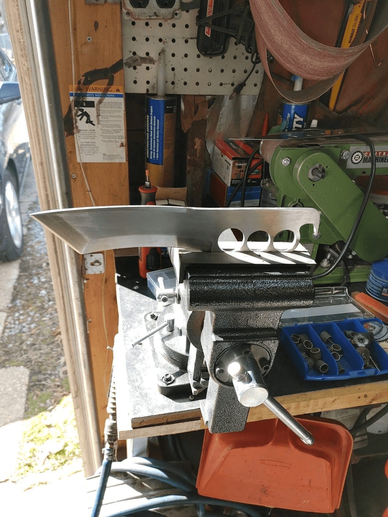 A custom handcrafted knife made by John, held in a workshop vise